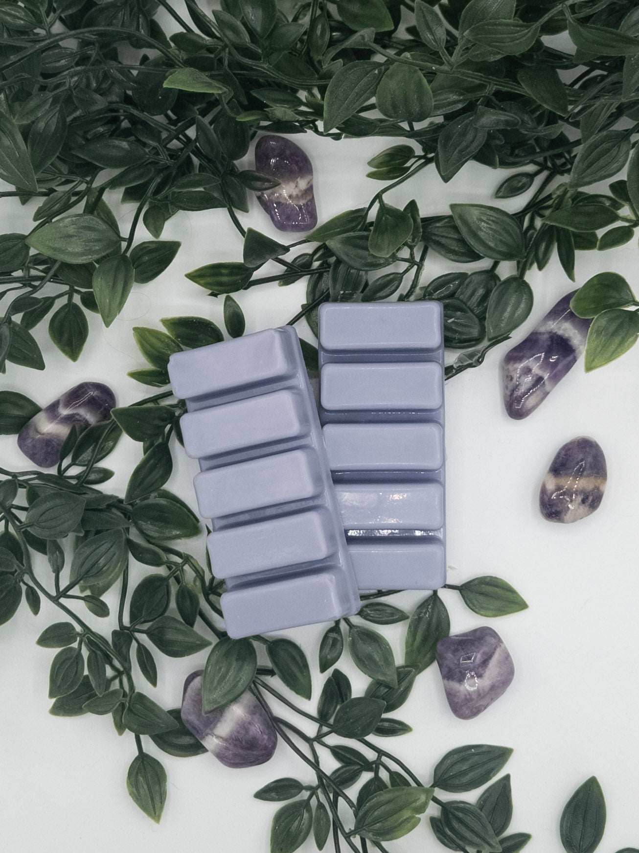 Purple wax melts in a mold surrounded by green leaves on a white surface