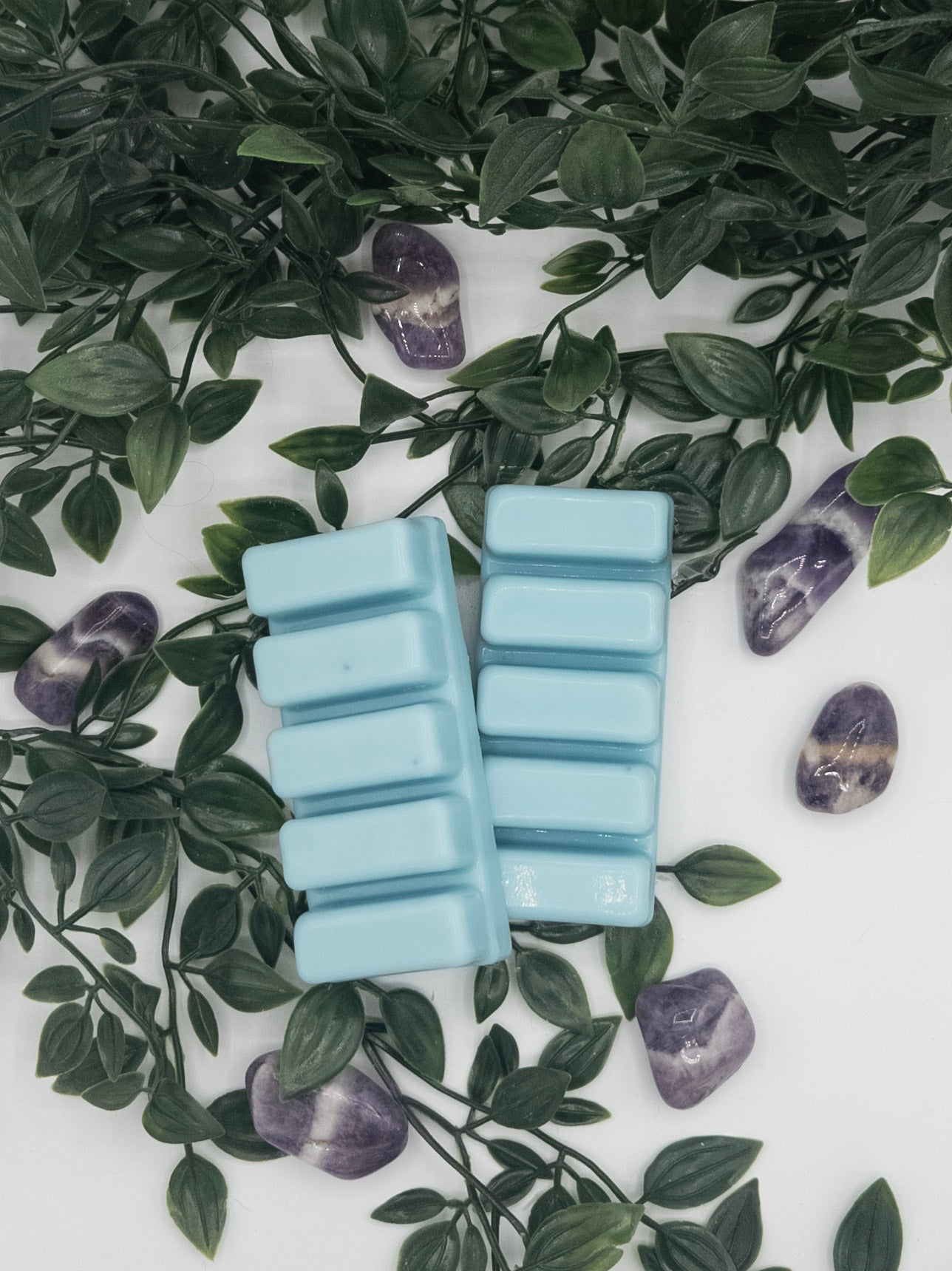 Blue wax melts on a white surface with green leaves and purple stones