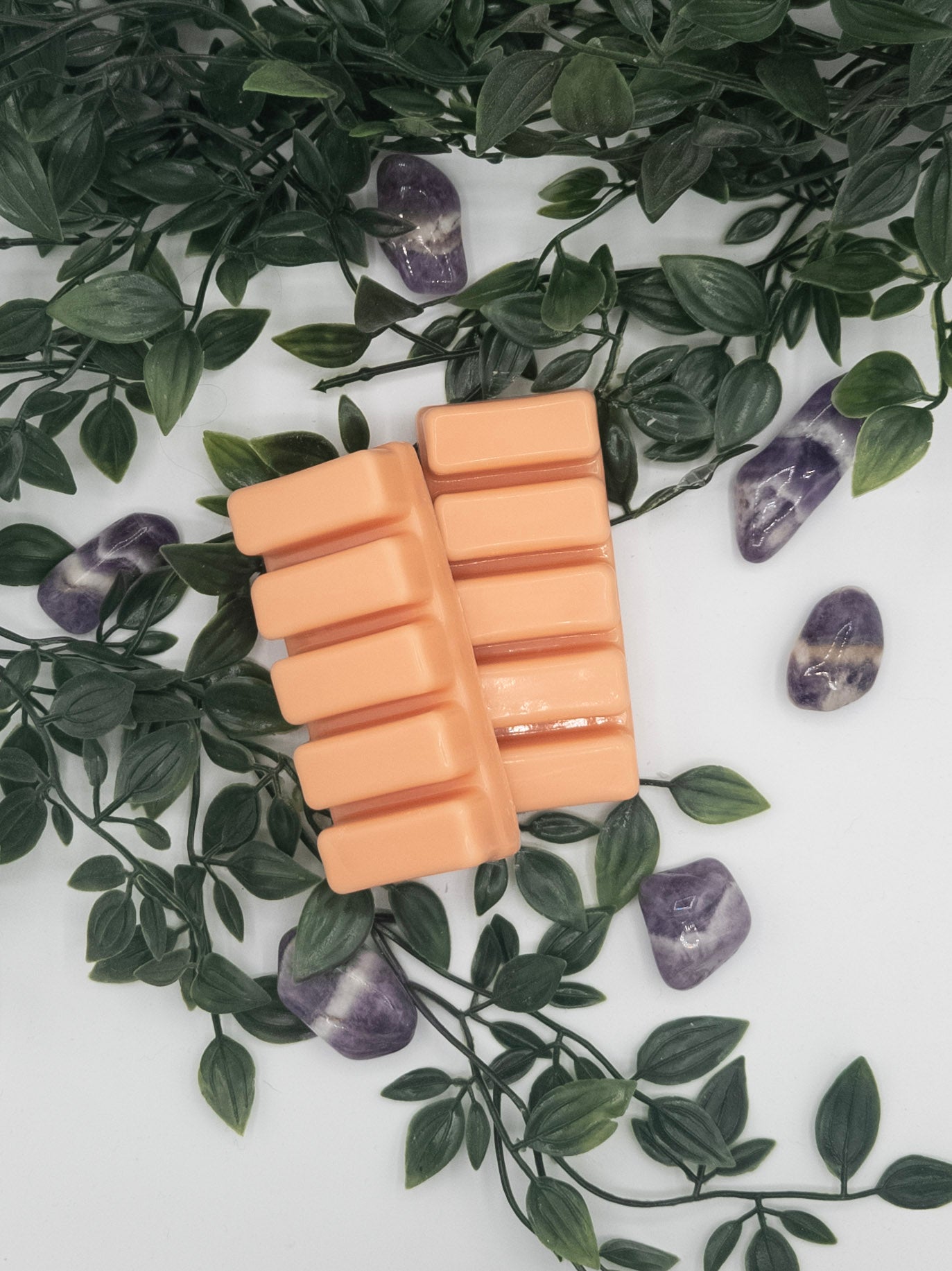 Rectangular peach-colored snap bar on a white surface with green leaves and Amethyst stones