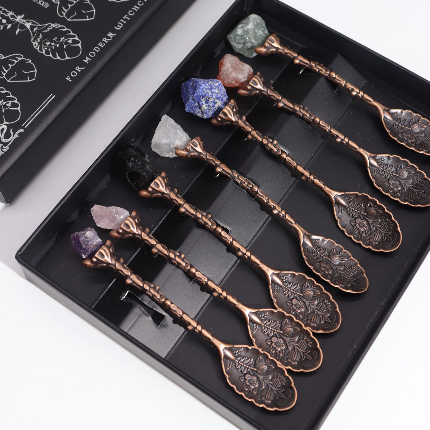 Set of decorative spoons with engraved designs on a black tray, featuring crystals on top.