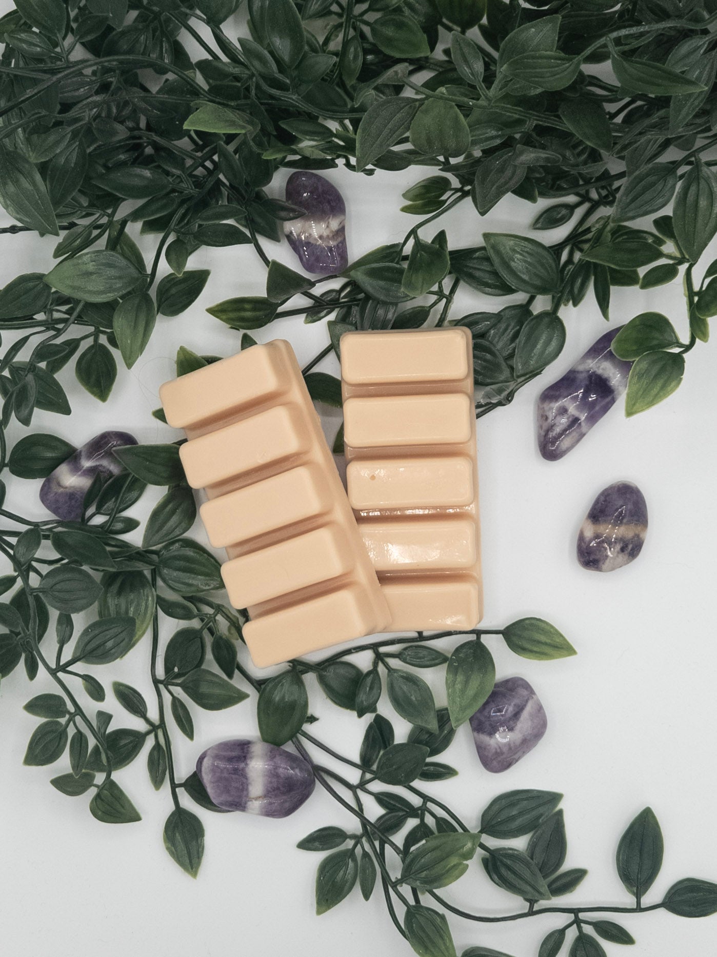 Two beige snap bars on a white surface with green leaves and Amethyst stones