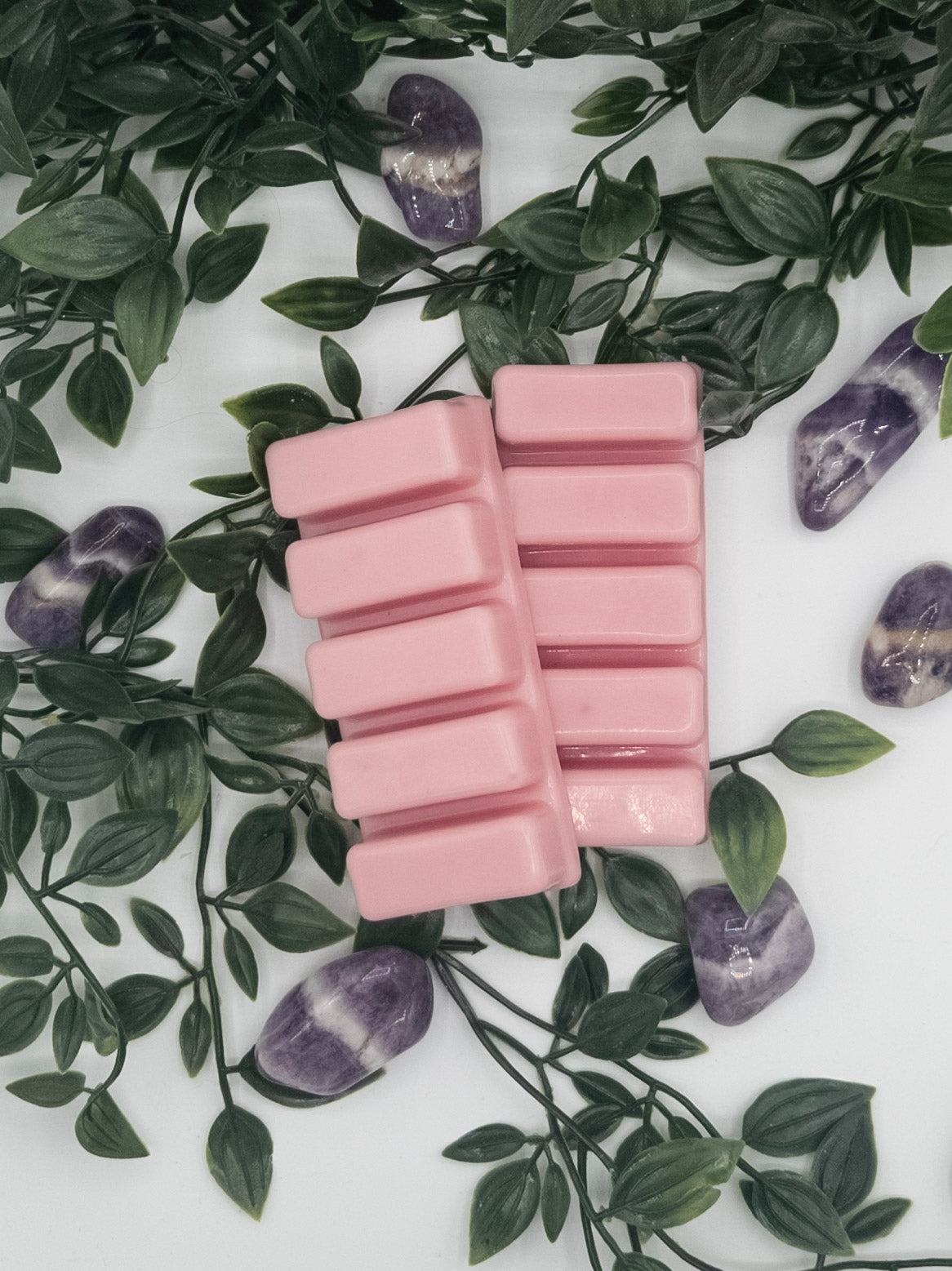 Pink wax melts on a white surface with green leaves and Amethyst stones