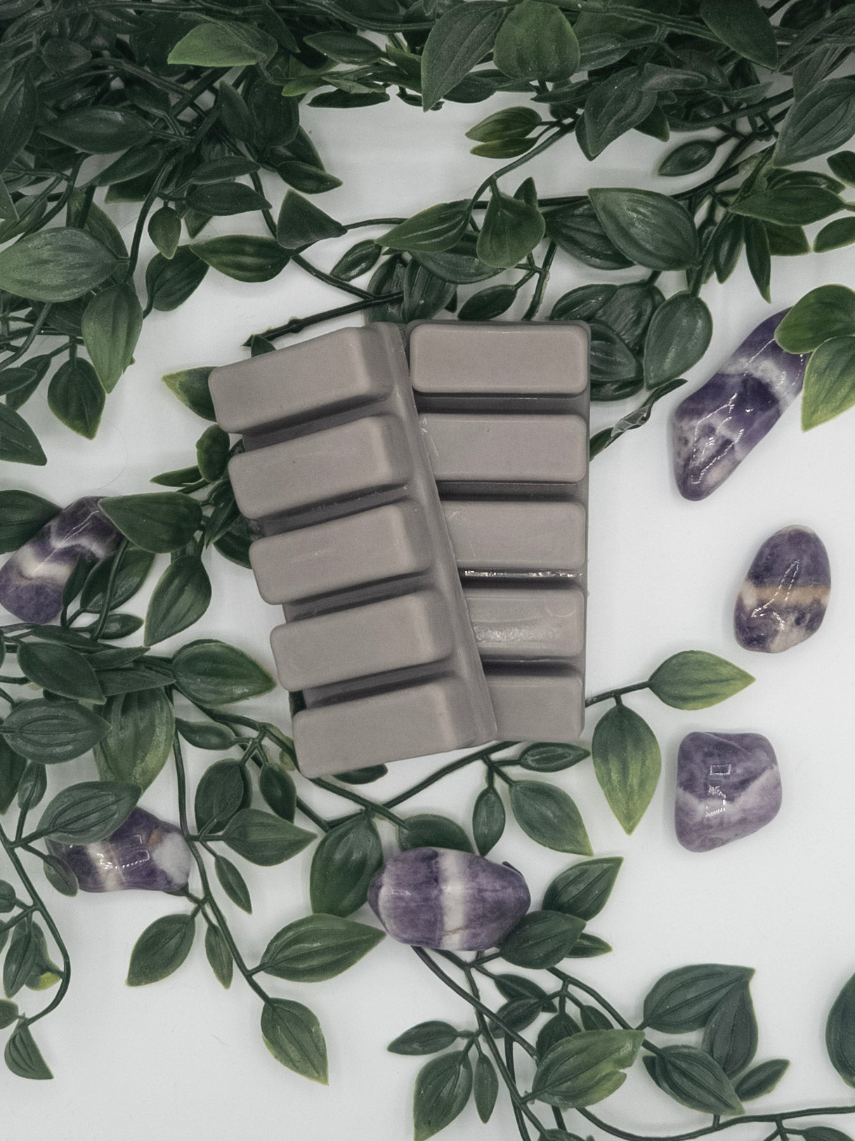 Gray wax melt snap bars on a white surface with green leaves and Amethyst stones.