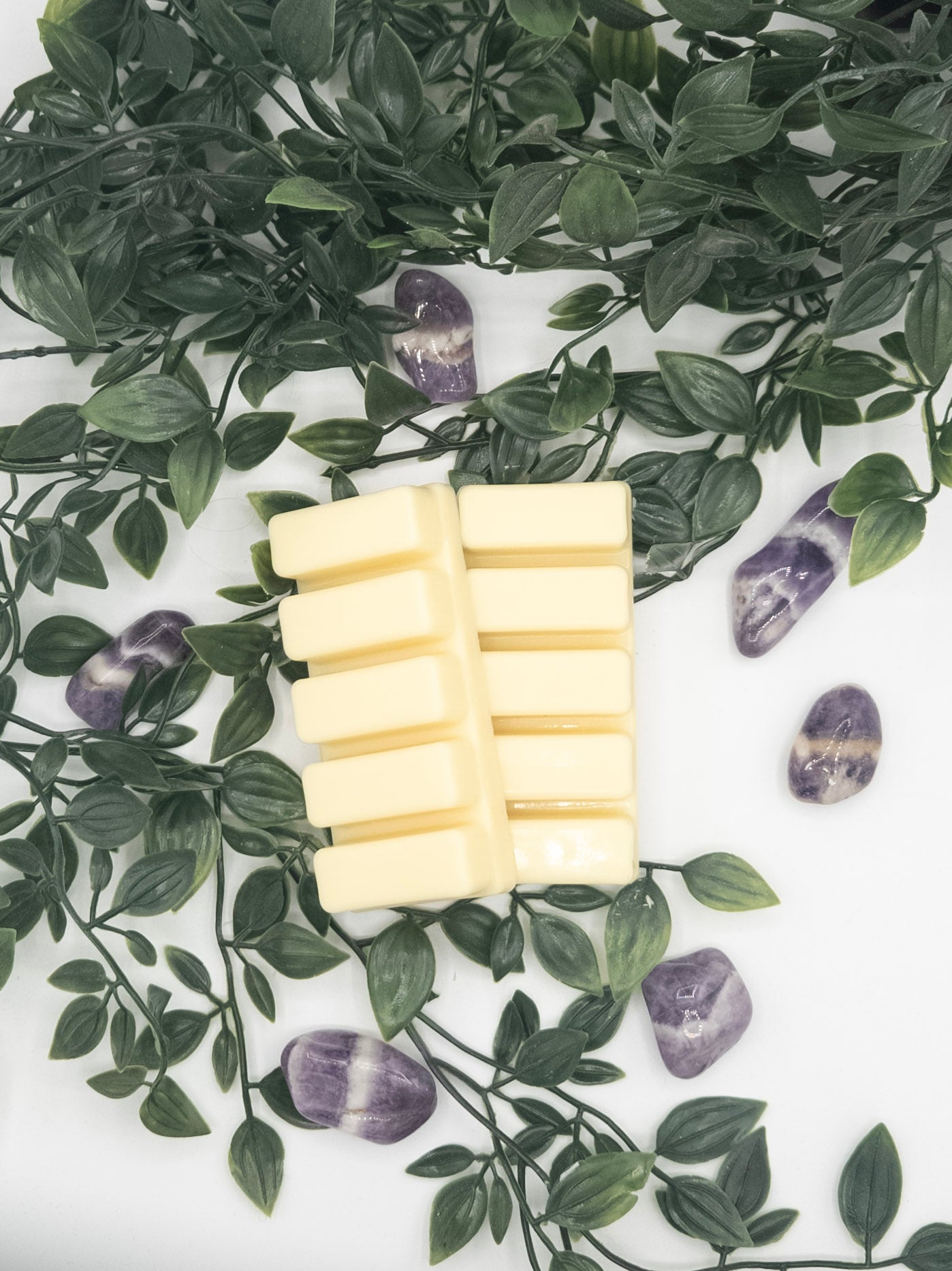 Two white snap bars on a white surface with green leaves and Amethyst in the background