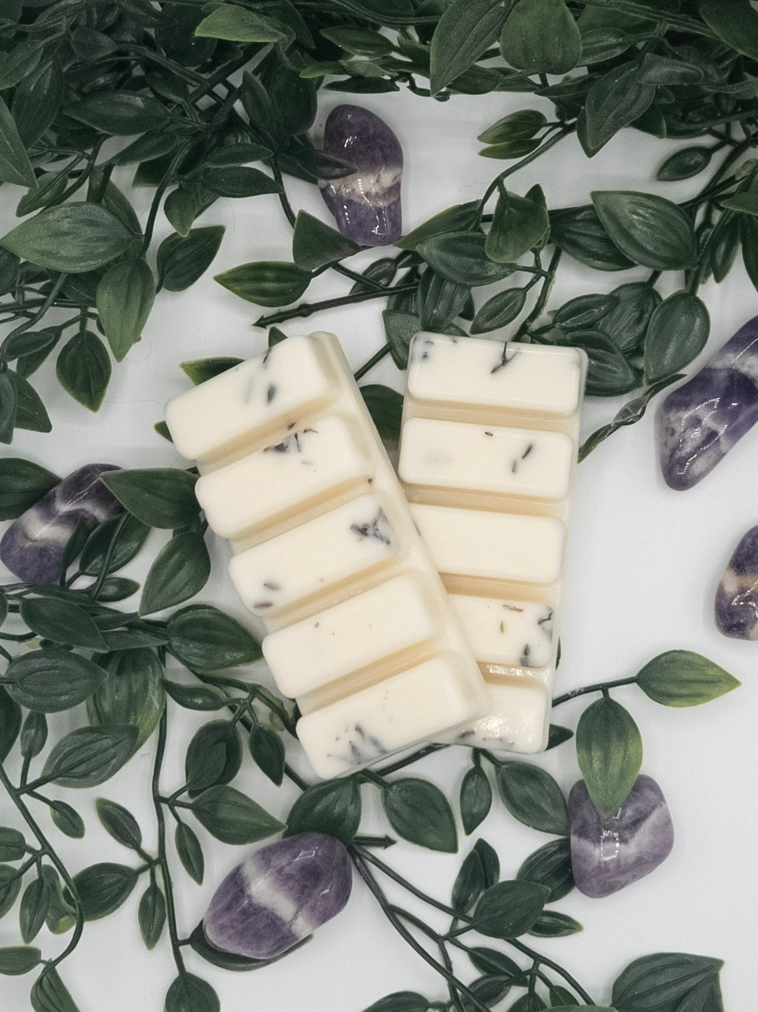White snap bars with lavender specks on a white surface with green leaves and Amethyst stones.
