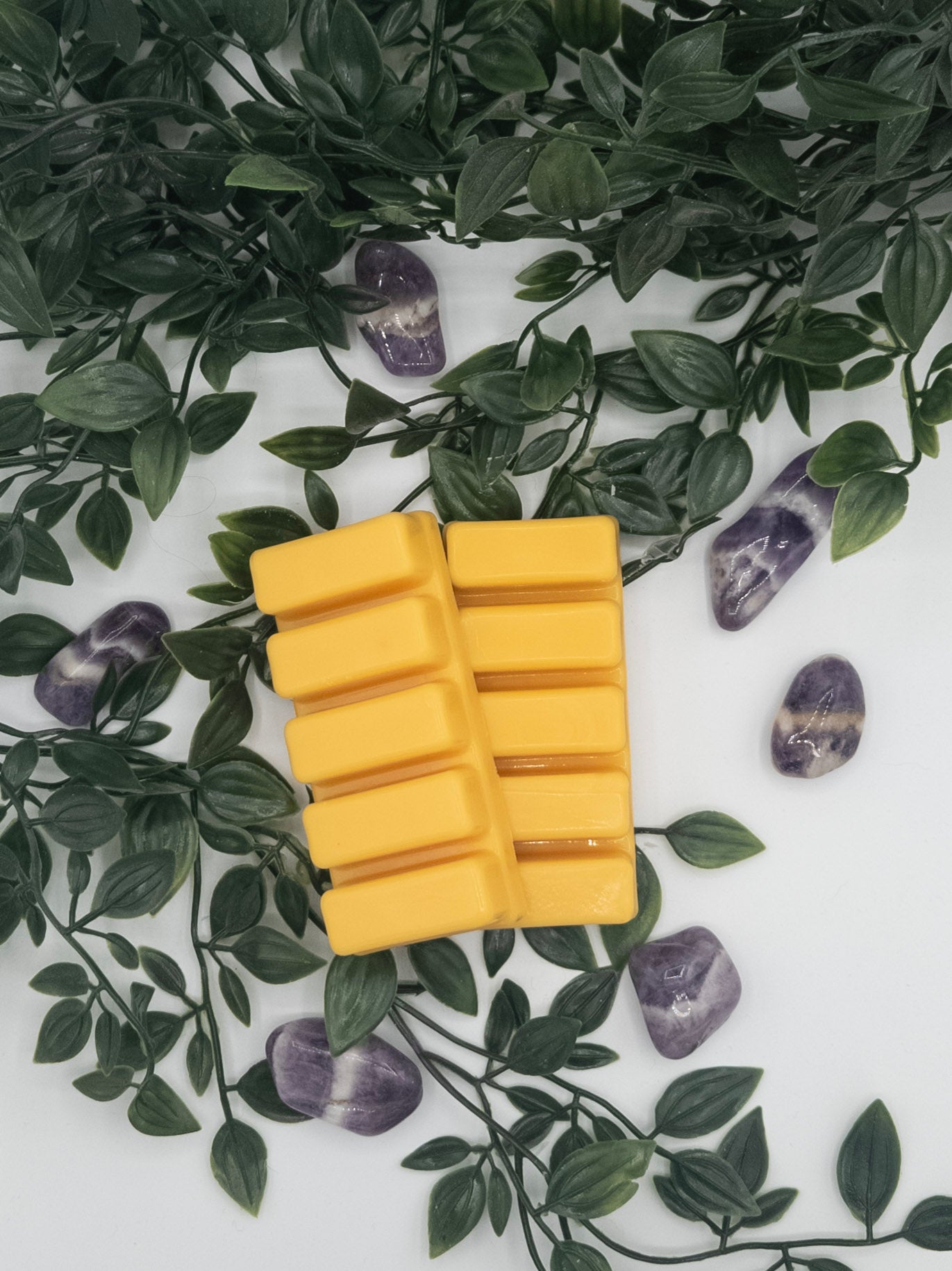 Yellow rectangular snap bar on a white surface with green leaves and Amethyst stones